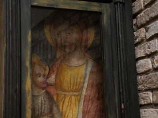 ‘An ancient painting, probably a fresco, depicting the Virgin Mary nursing the infant Jesus (the “Madonna del Latte” motif). The work, characterised by warm colours, is protected by a glass panel and set within a dark wooden frame of austere design, all mounted on a rustic exposed brick wall.’