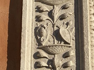 A decorative stone relief featuring carved plant and animal motifs, set vertically on a façade.